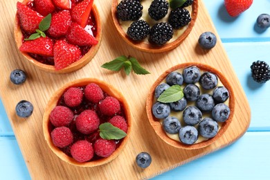 Photo of Tartlets with different fresh berries on light blue wooden table, flat lay. Delicious dessert
