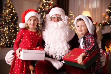 Photo of Santa Claus and little children with presents in room decorated for Christmas