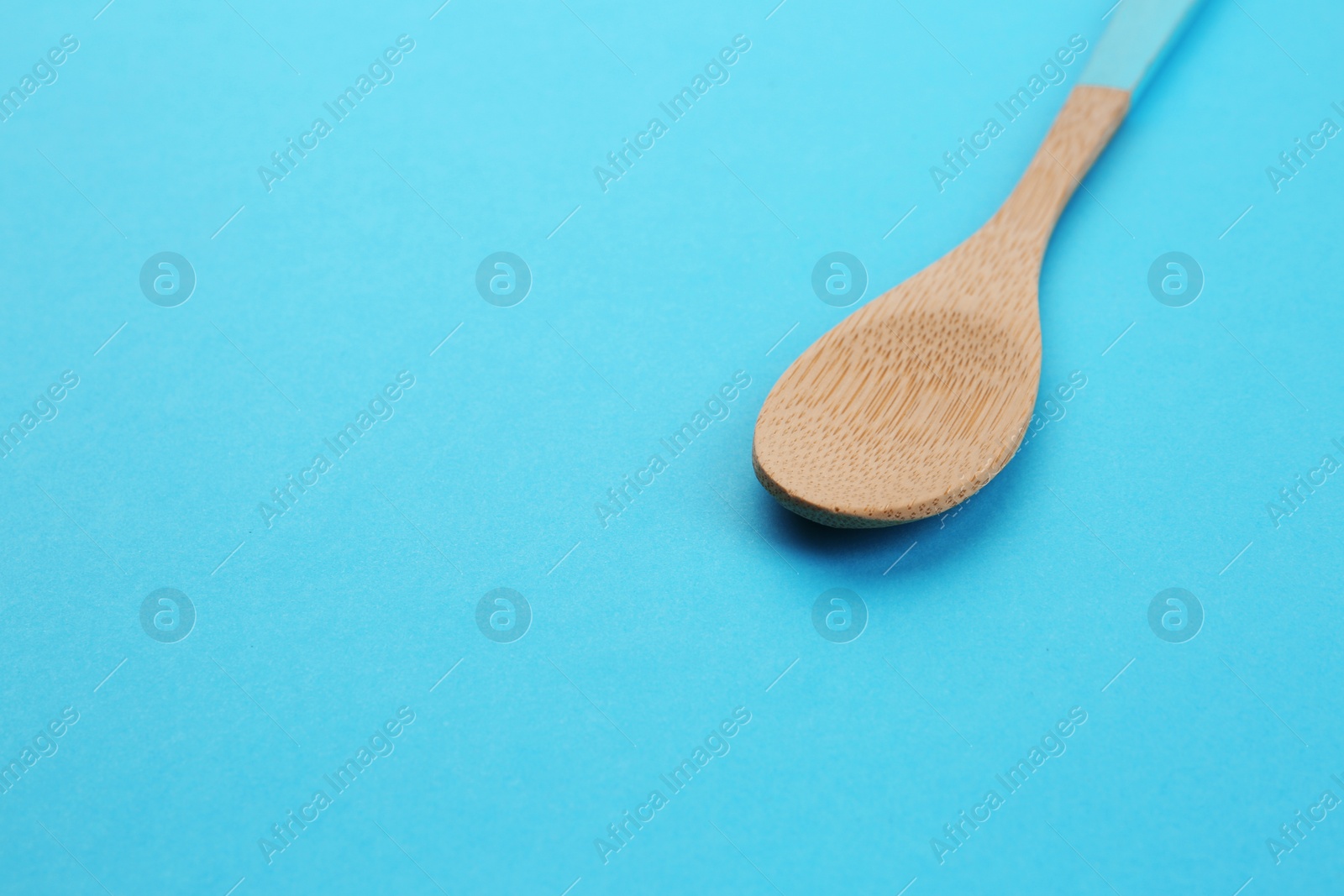 Photo of Clean empty bamboo spoon on blue background, space for text