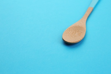 Clean empty bamboo spoon on blue background, space for text