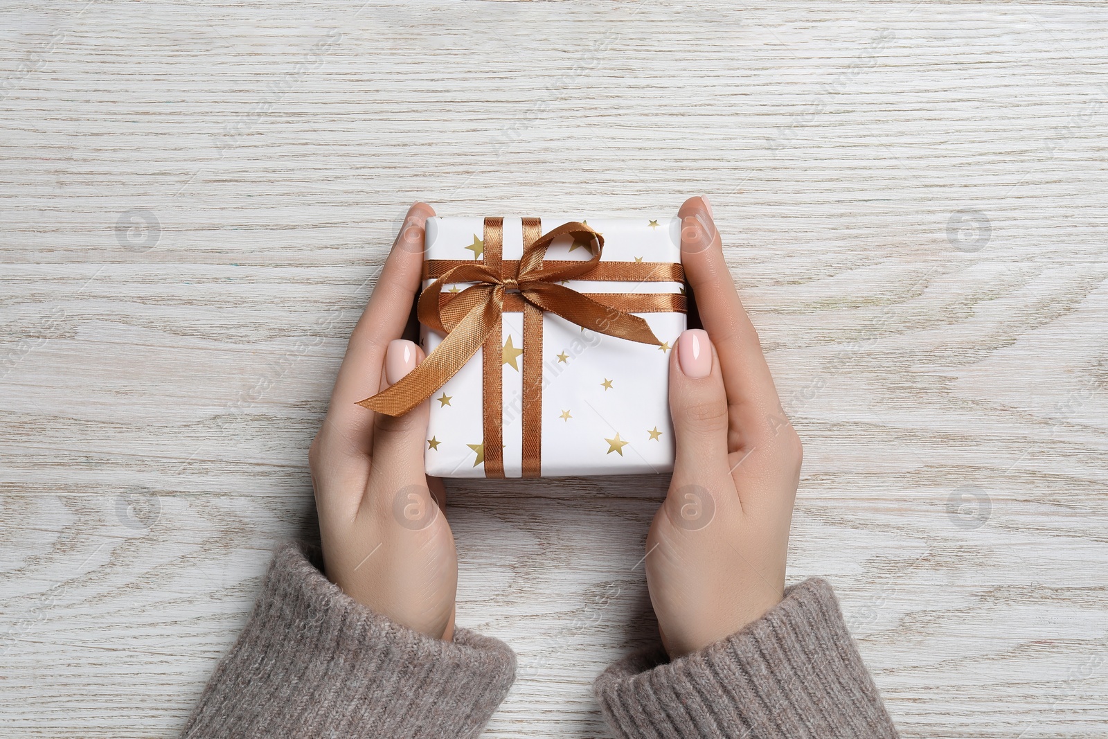 Photo of Christmas present. Woman holding gift box on white wooden background, top view