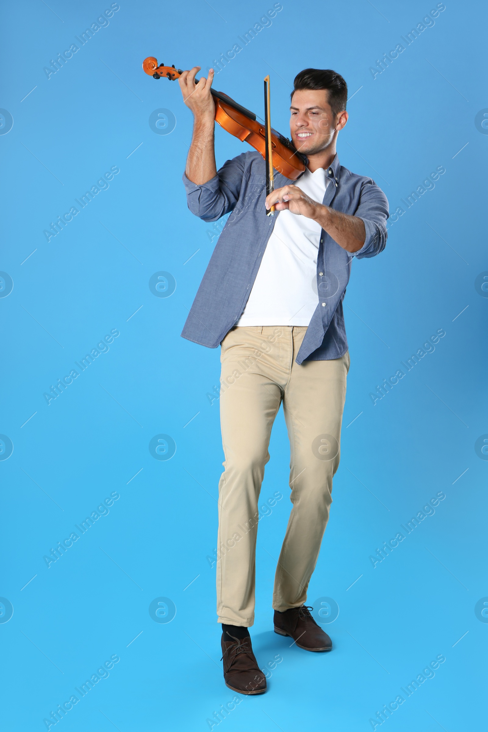 Photo of Happy man playing violin on light blue background