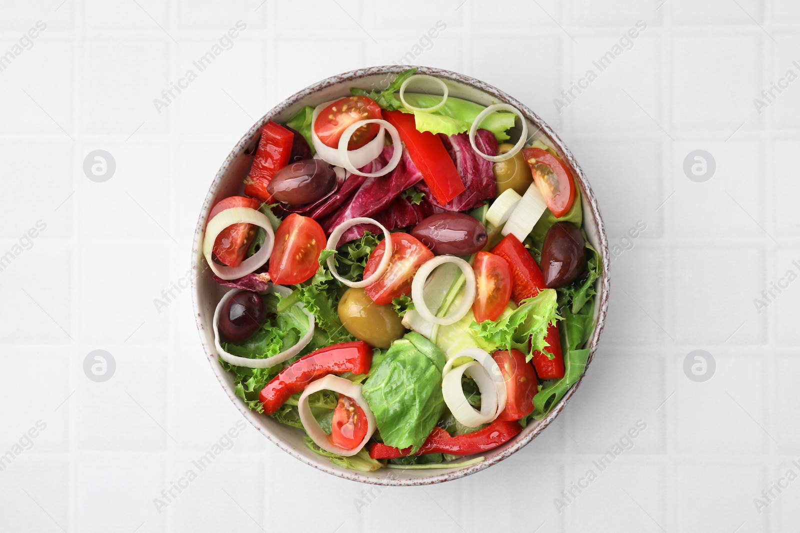 Photo of Bowl of tasty salad with leek and olives on white tiled table, top view