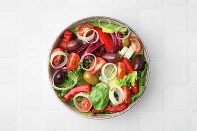 Bowl of tasty salad with leek and olives on white tiled table, top view