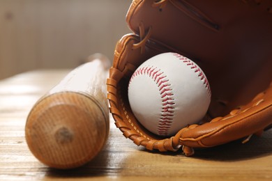 Photo of Baseball glove, bat and ball on wooden table, closeup