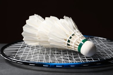 Feather badminton shuttlecocks and racket on grey table against black background, closeup