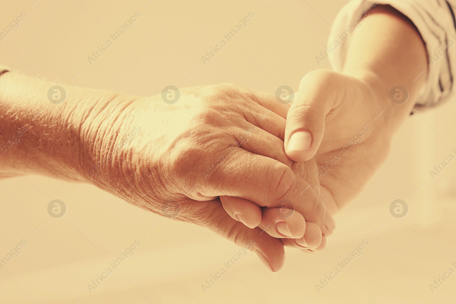 Image of Helping hands on beige background, closeup. Elderly care concept