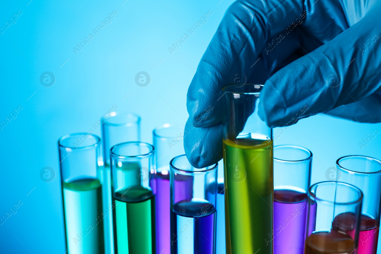Photo of Scientist taking test tube with liquid on light blue background, closeup