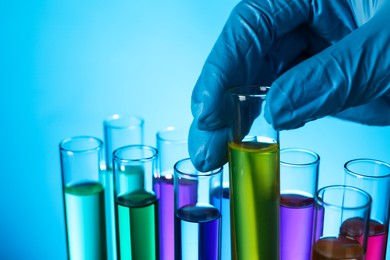 Photo of Scientist taking test tube with liquid on light blue background, closeup
