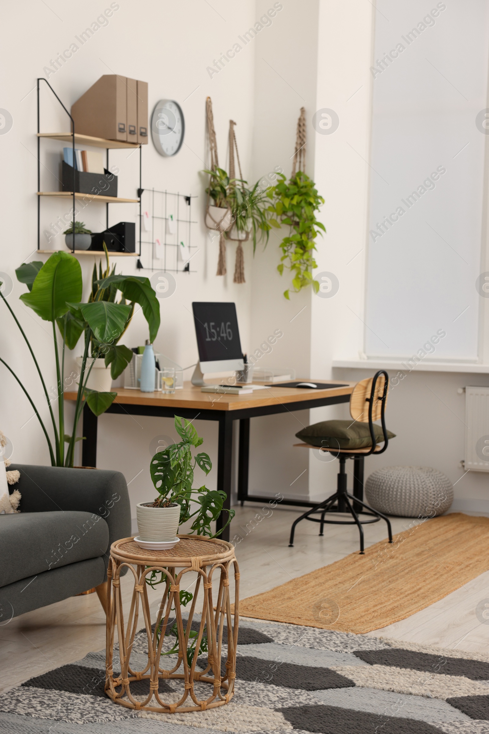 Photo of Cozy workplace with computer, modern furniture and houseplants at home