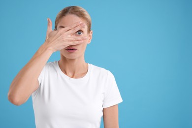 Photo of Embarrassed woman covering face on light blue background. Space for text