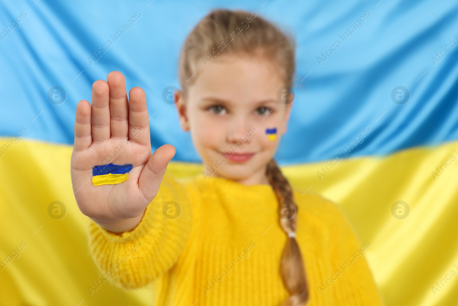 Photo of Little girl with paint on hand and face near Ukrainian flag, focus on palm