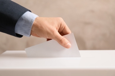 Man putting his vote into ballot box on color background, closeup