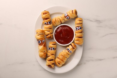 Photo of Plate with tasty sausage mummies for Halloween party and ketchup on white marble table, top view