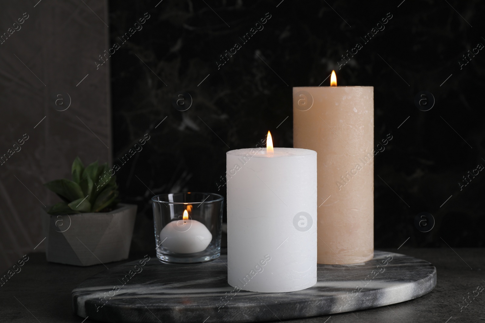 Photo of Marble board with burning candles on dark table