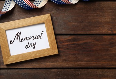 Photo of Frame with phrase Memorial Day and ribbon on wooden table, flat lay. Space for text