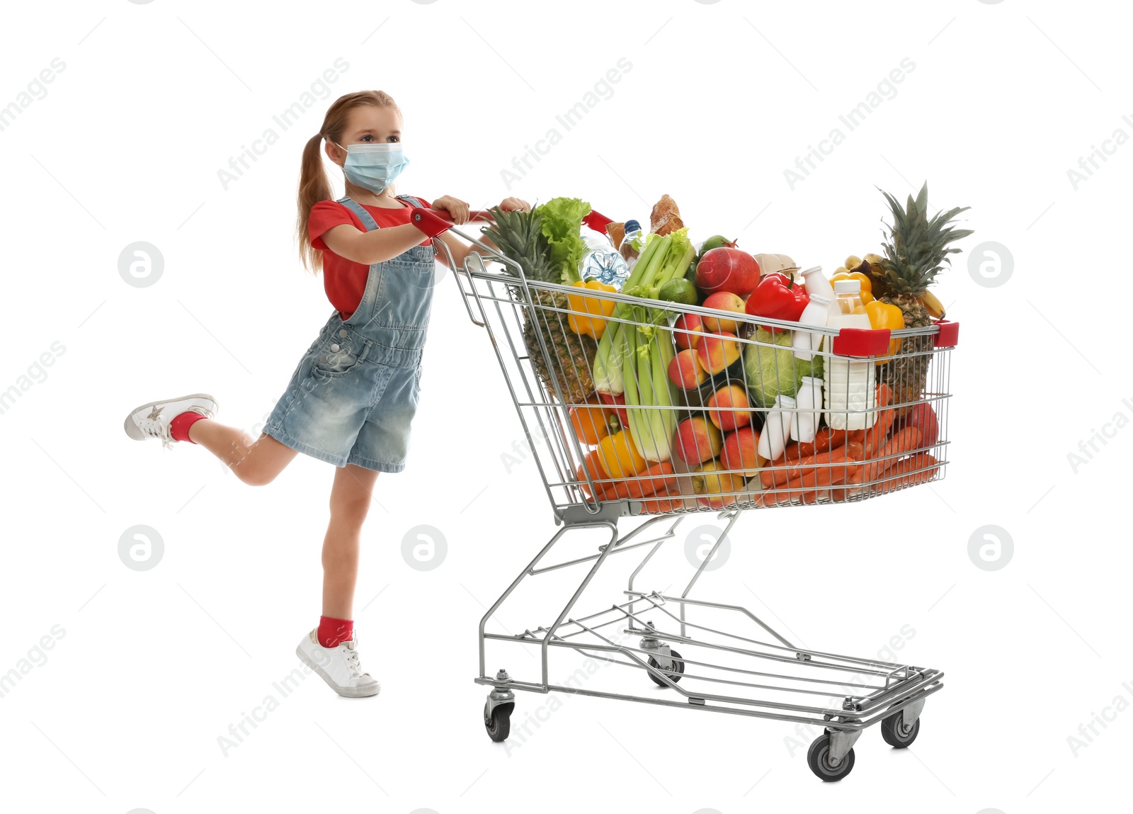 Photo of Little girl in medical mask with shopping cart full of groceries on white background