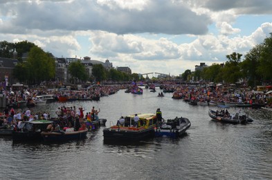 Photo of AMSTERDAM, NETHERLANDS - AUGUST 06, 2022: Many people in boats at LGBT pride parade on river