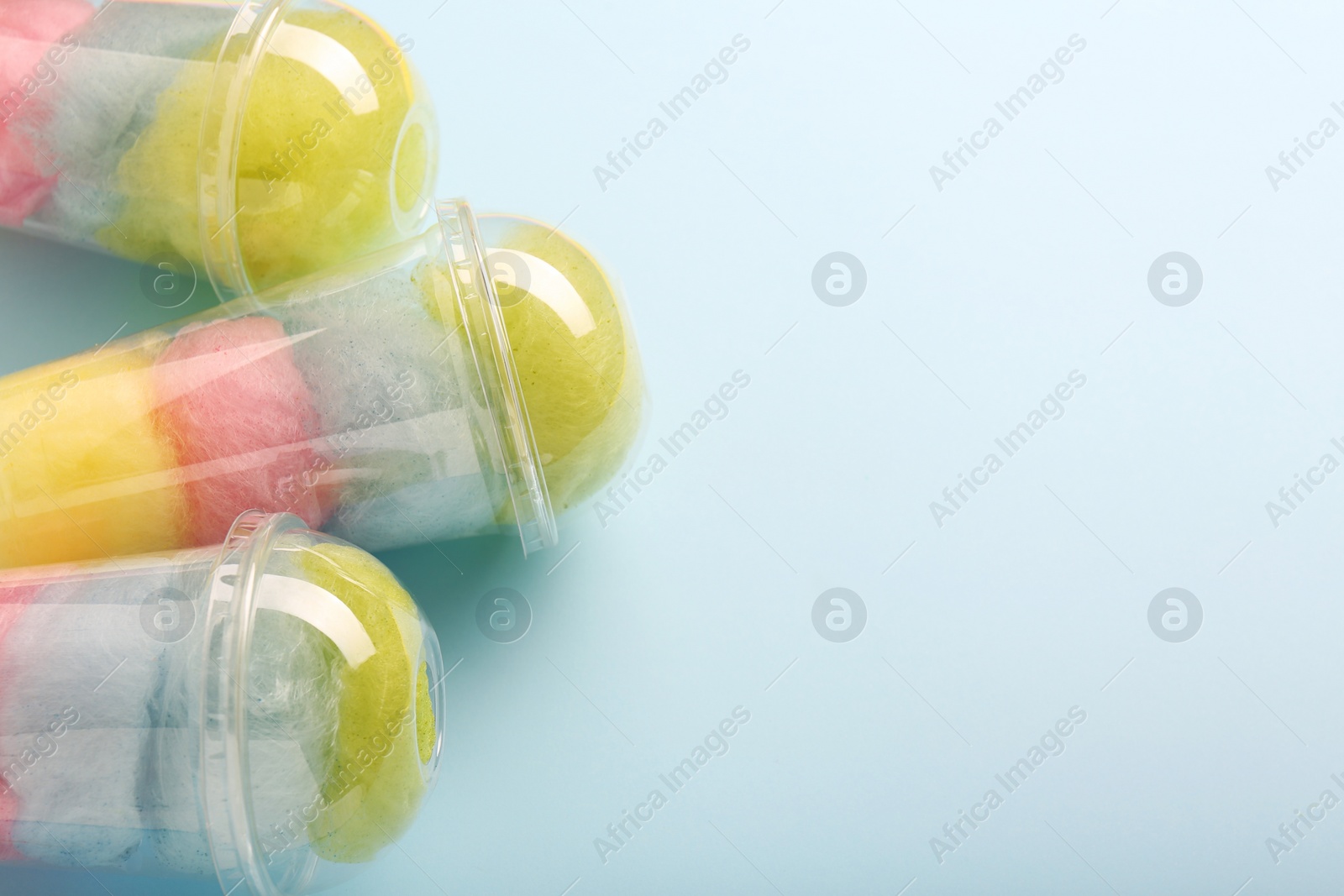 Photo of Colorful cotton candies in plastic cups on light blue background, flat lay. Space for text