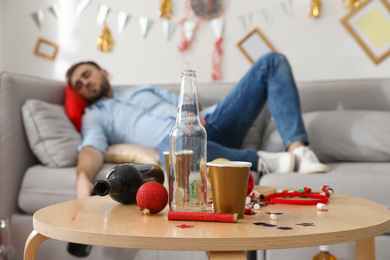 Photo of Drunk man sleeping in room after New Year party, focus on messy table