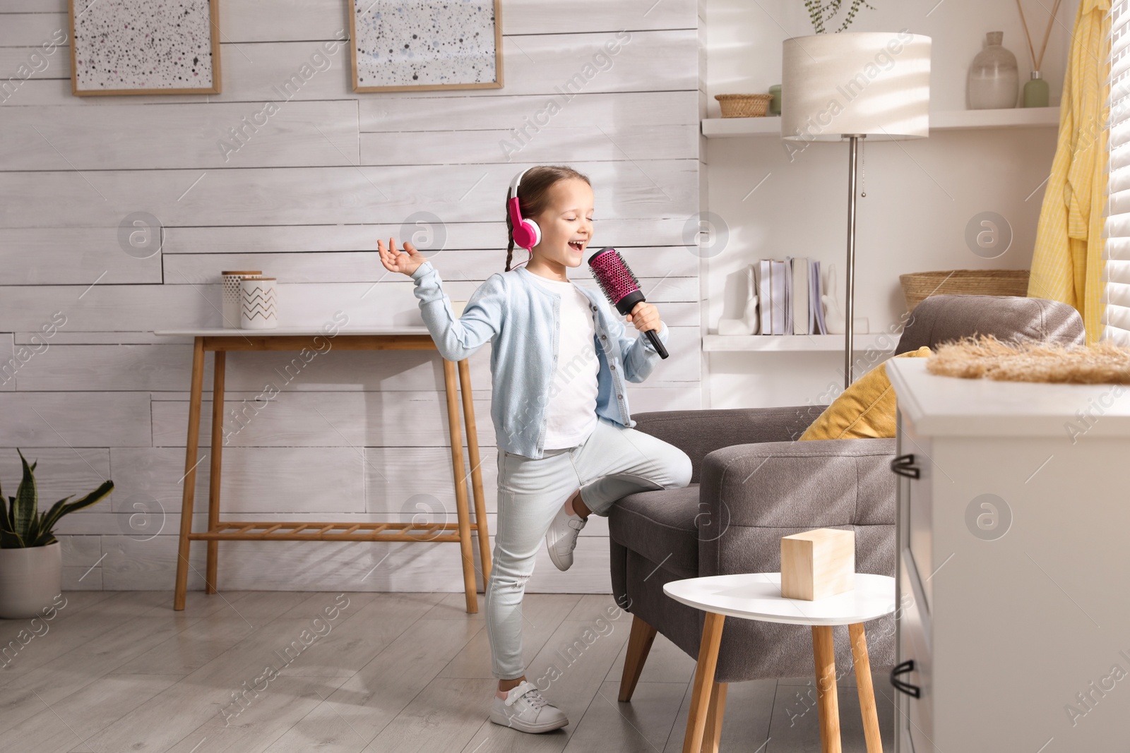 Photo of Cute little girl in headphones with hairbrush singing at home