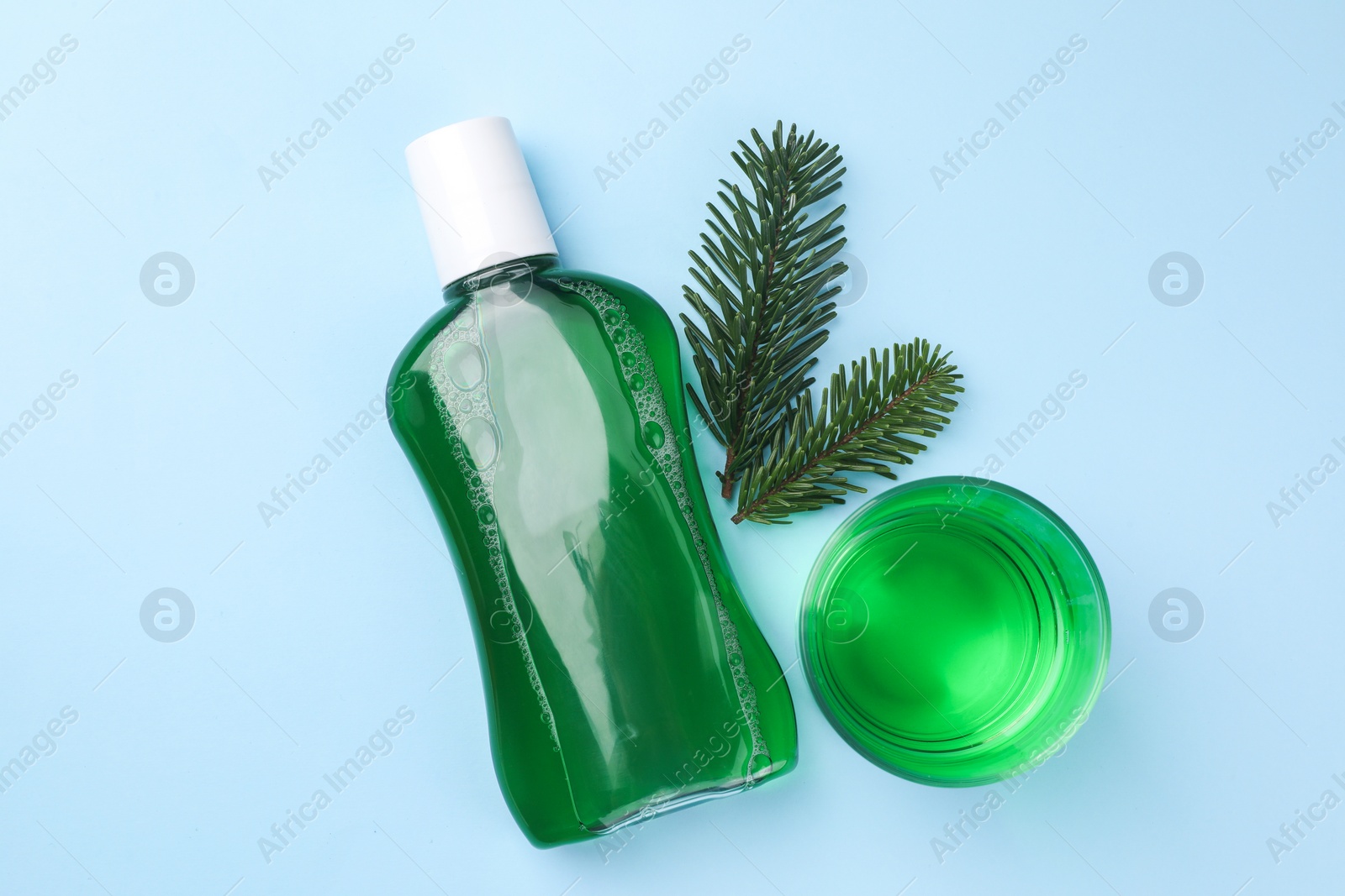 Photo of Fresh mouthwash in bottle, glass and fir branches on light blue background, flat lay