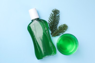 Fresh mouthwash in bottle, glass and fir branches on light blue background, flat lay