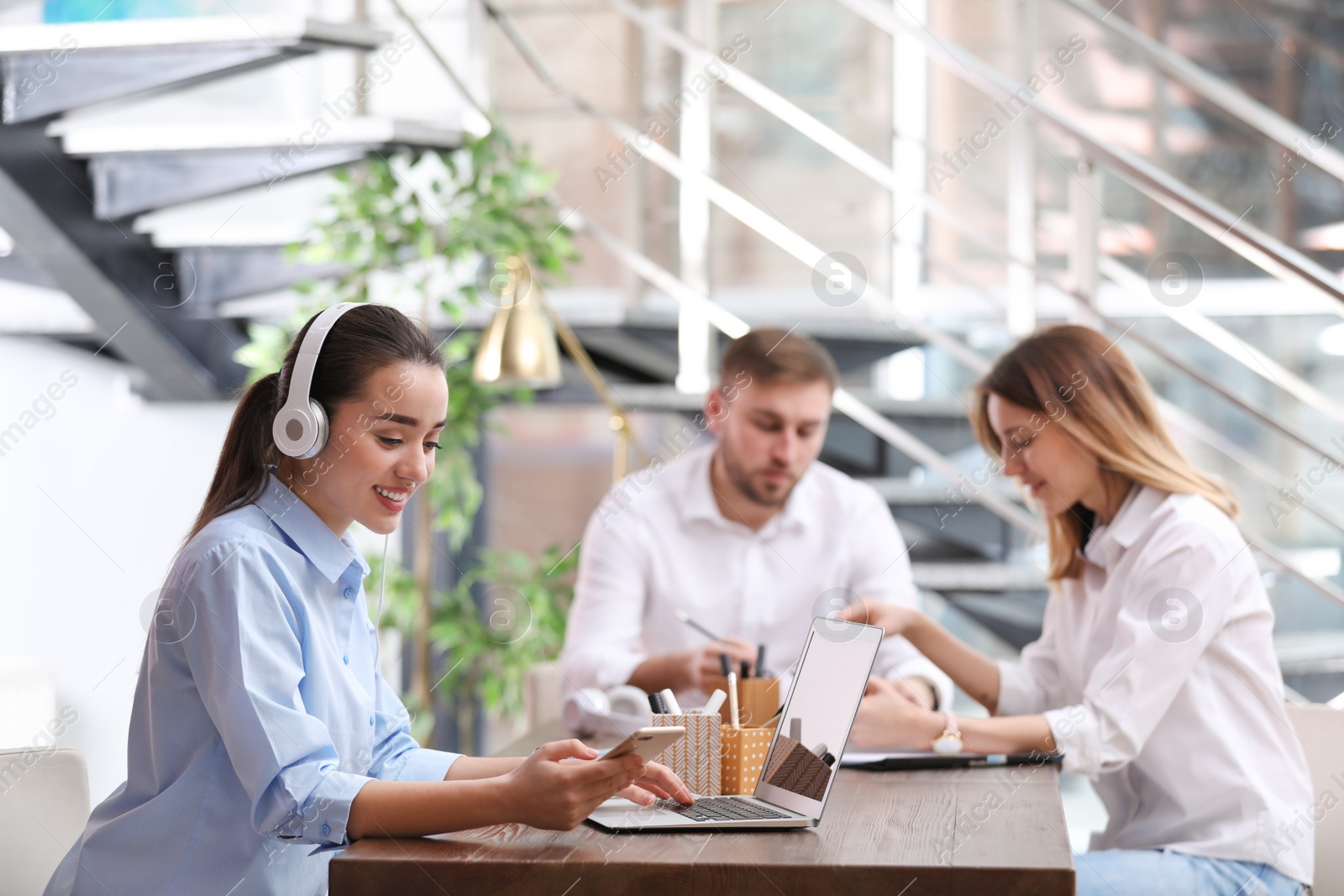 Photo of Young businesswoman with headphones, laptop and her colleagues at table in office