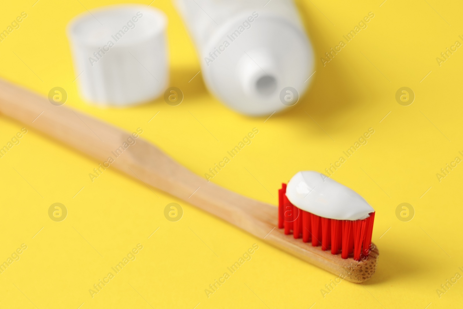 Photo of Wooden brush with toothpaste on yellow background, closeup