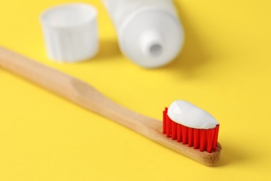 Photo of Wooden brush with toothpaste on yellow background, closeup