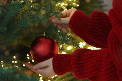 Woman decorating Christmas tree with red festive ball, closeup