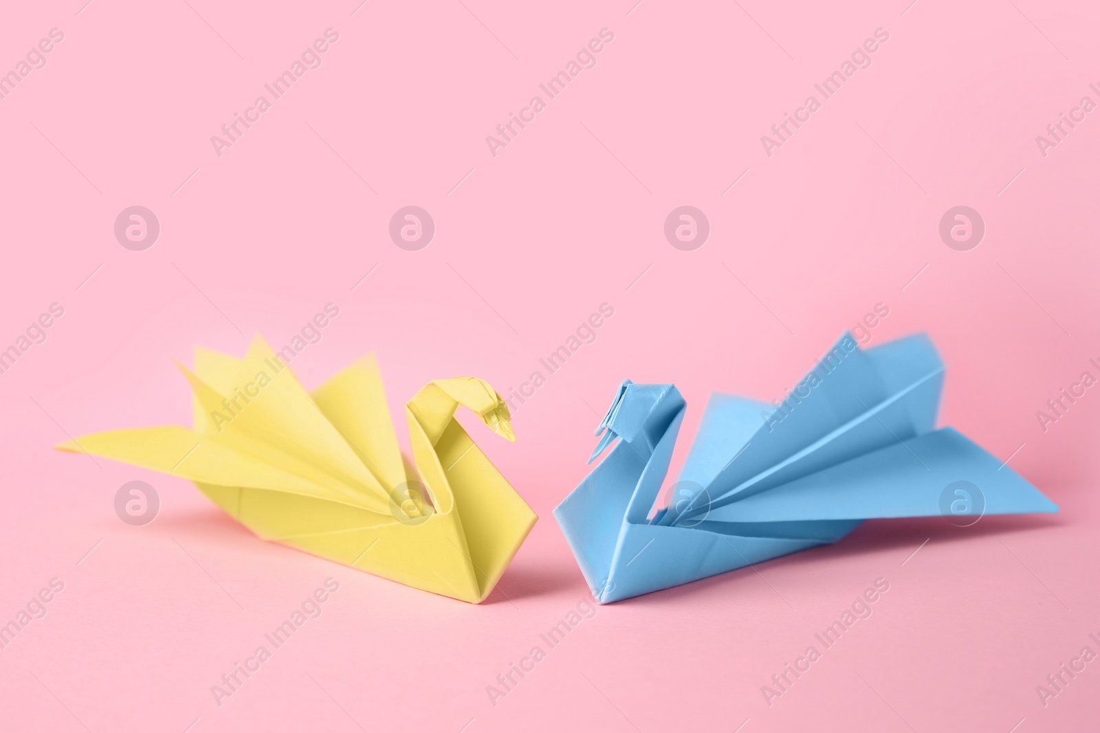 Photo of Origami art. Beautiful paper swans on pink background