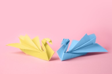 Photo of Origami art. Beautiful paper swans on pink background