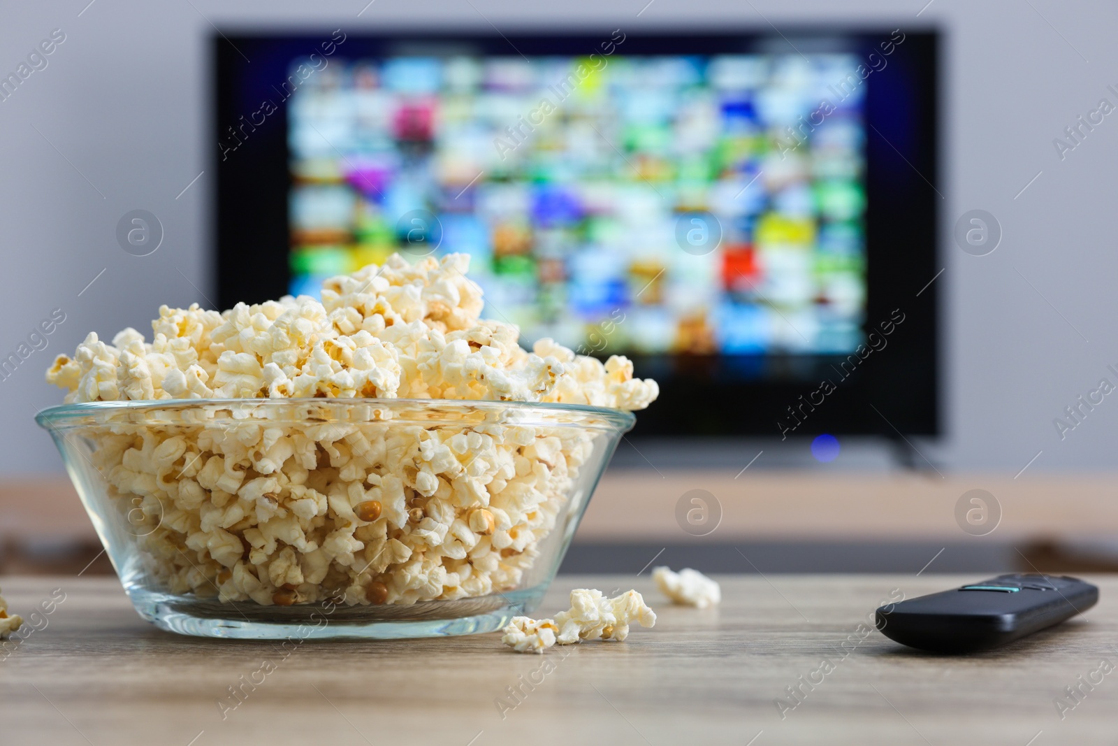 Photo of Bowl of popcorn and TV remote control on table indoors