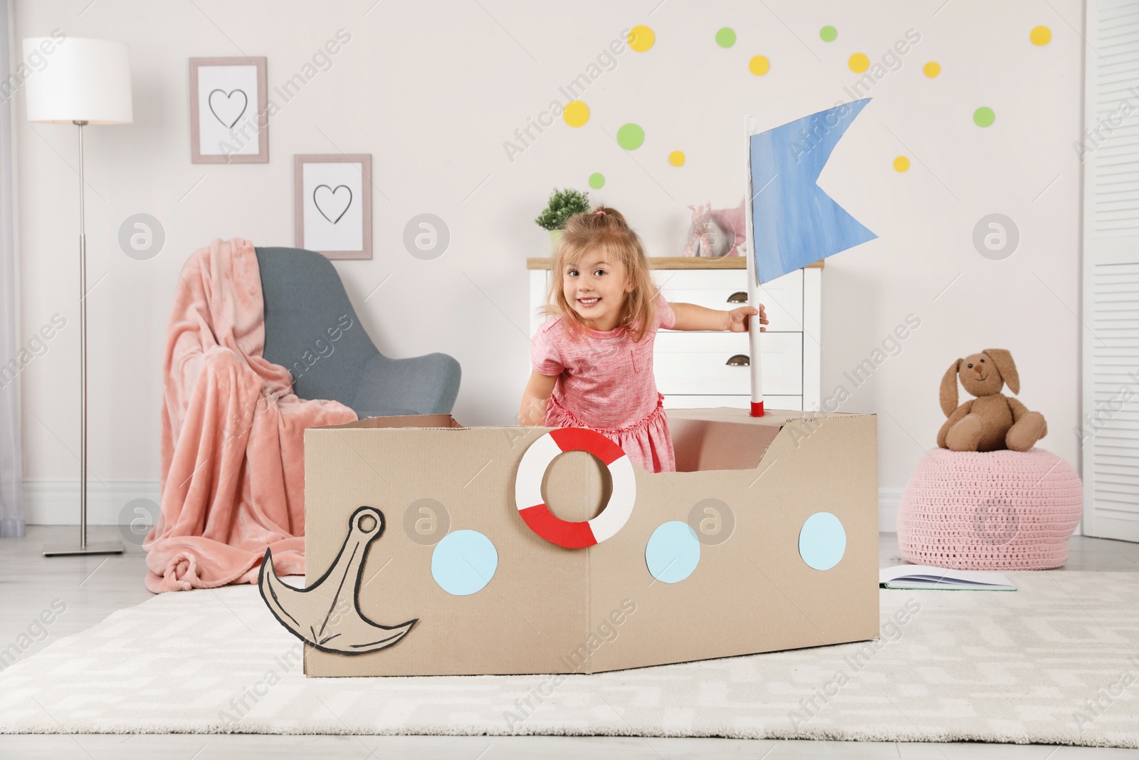 Photo of Cute little girl playing with cardboard ship at home