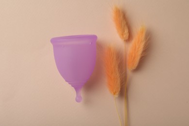 Photo of Menstrual cup and dry flowers on beige background, flat lay