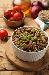 Delicious lentils with bacon and green onion in bowl served on wooden table