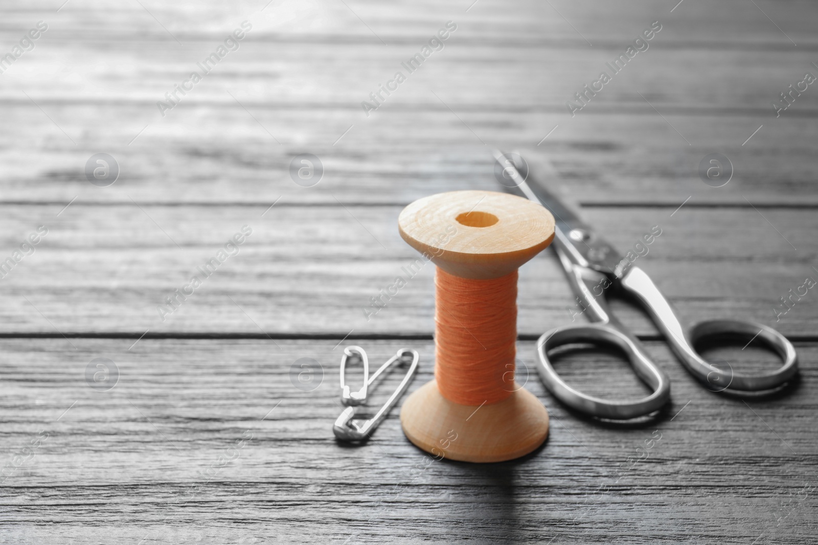 Photo of Spool of thread, scissors and pins on wooden background. Tailoring equipment