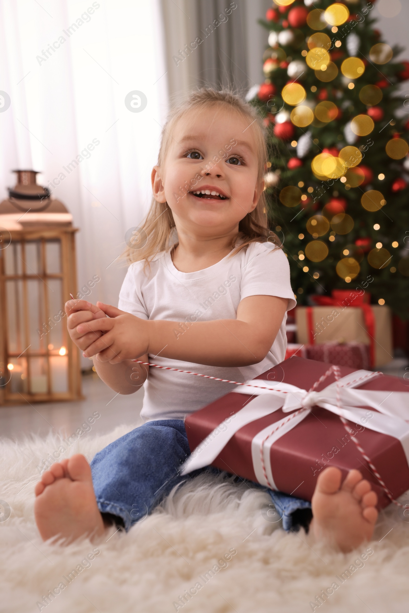 Photo of Cute little girl with Christmas gift in festively decorated room