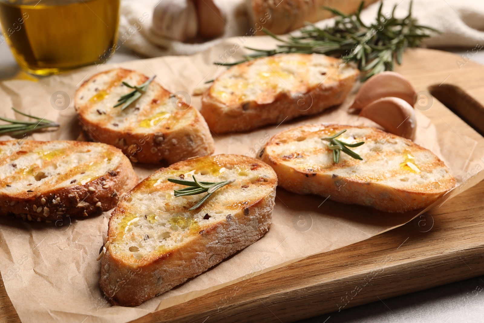 Photo of Tasty bruschettas with oil and rosemary on wooden board, closeup