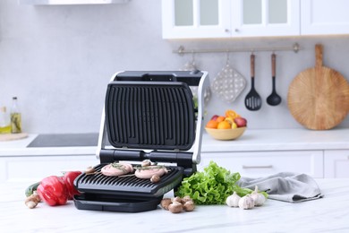 Electric grill with homemade sausages, rosemary and vegetables on white table in kitchen