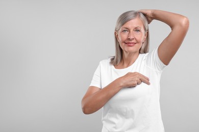Photo of Beautiful senior woman doing breast self-examination on light grey background, space for text