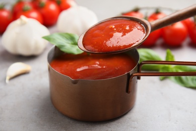 Photo of Spoon with tomato sauce over pan on grey table