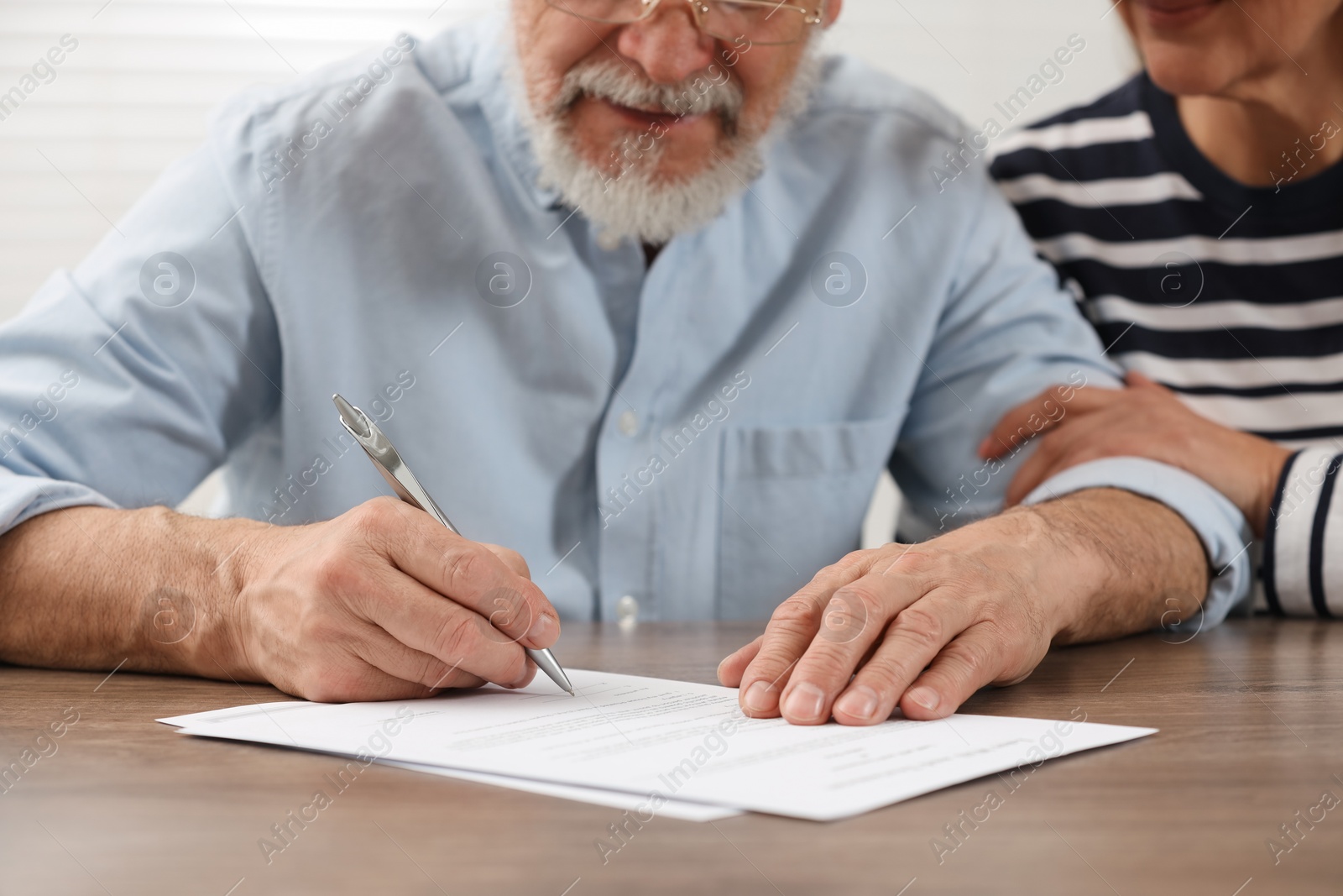 Photo of Senior couple signing Last Will and Testament at wooden table, closeup