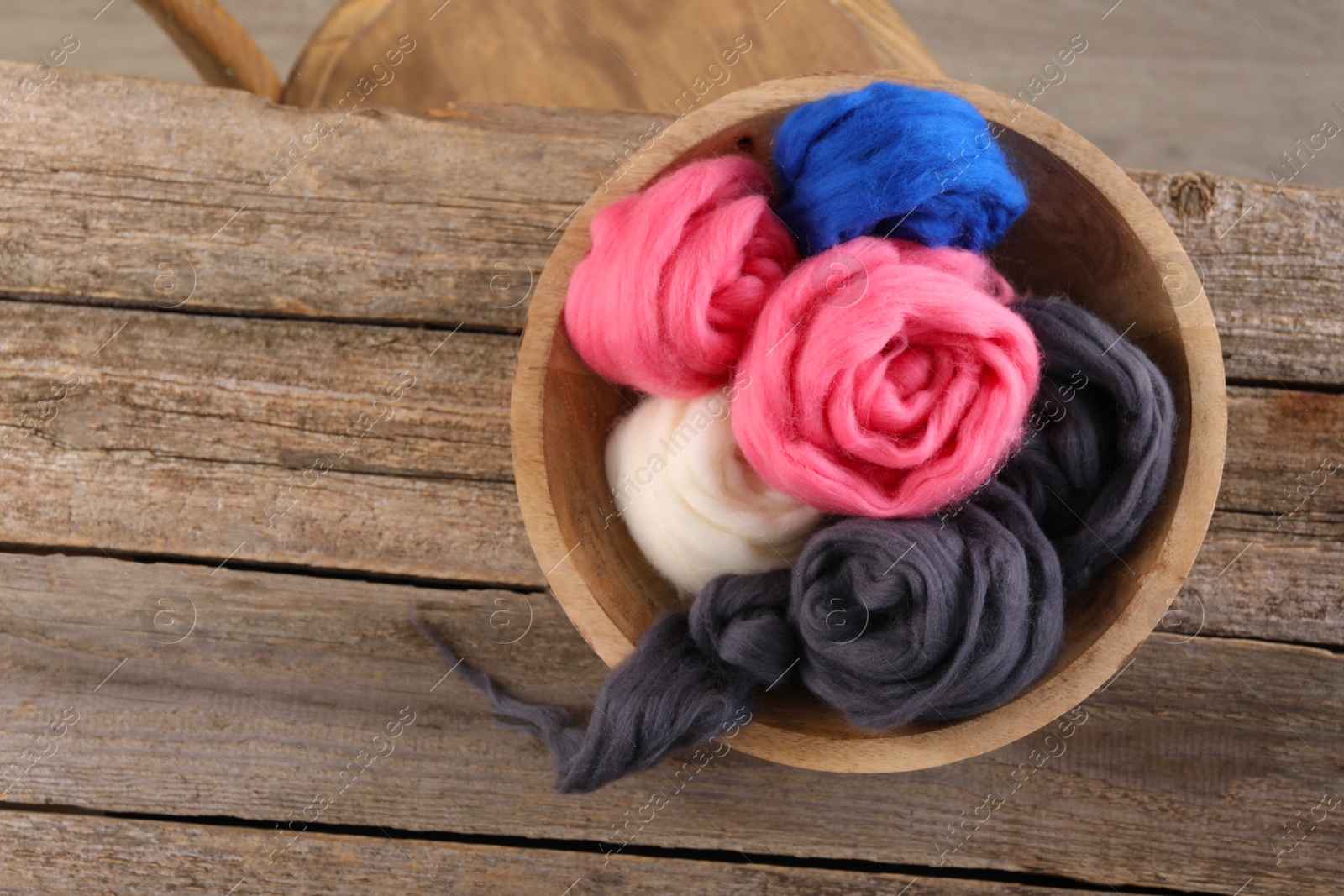 Photo of Colorful felting wool in bowl on wooden table, top view. Space for text