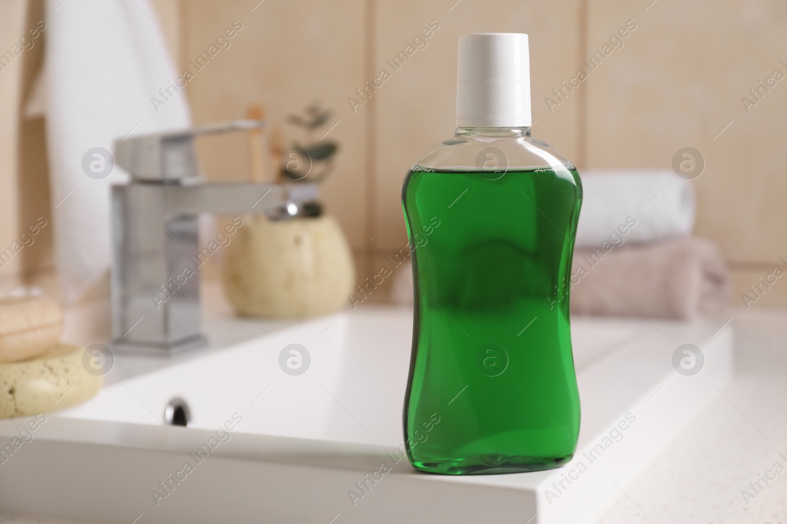 Photo of Fresh mouthwash in bottle on sink in bathroom, closeup. Space for text