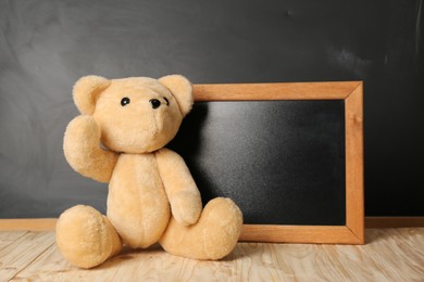 Photo of Teddy bear and small blackboard on wooden table. Space for text