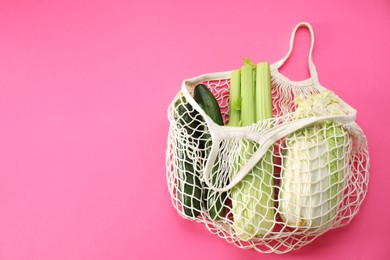 String bag with different vegetables on bright pink background, top view. Space for text