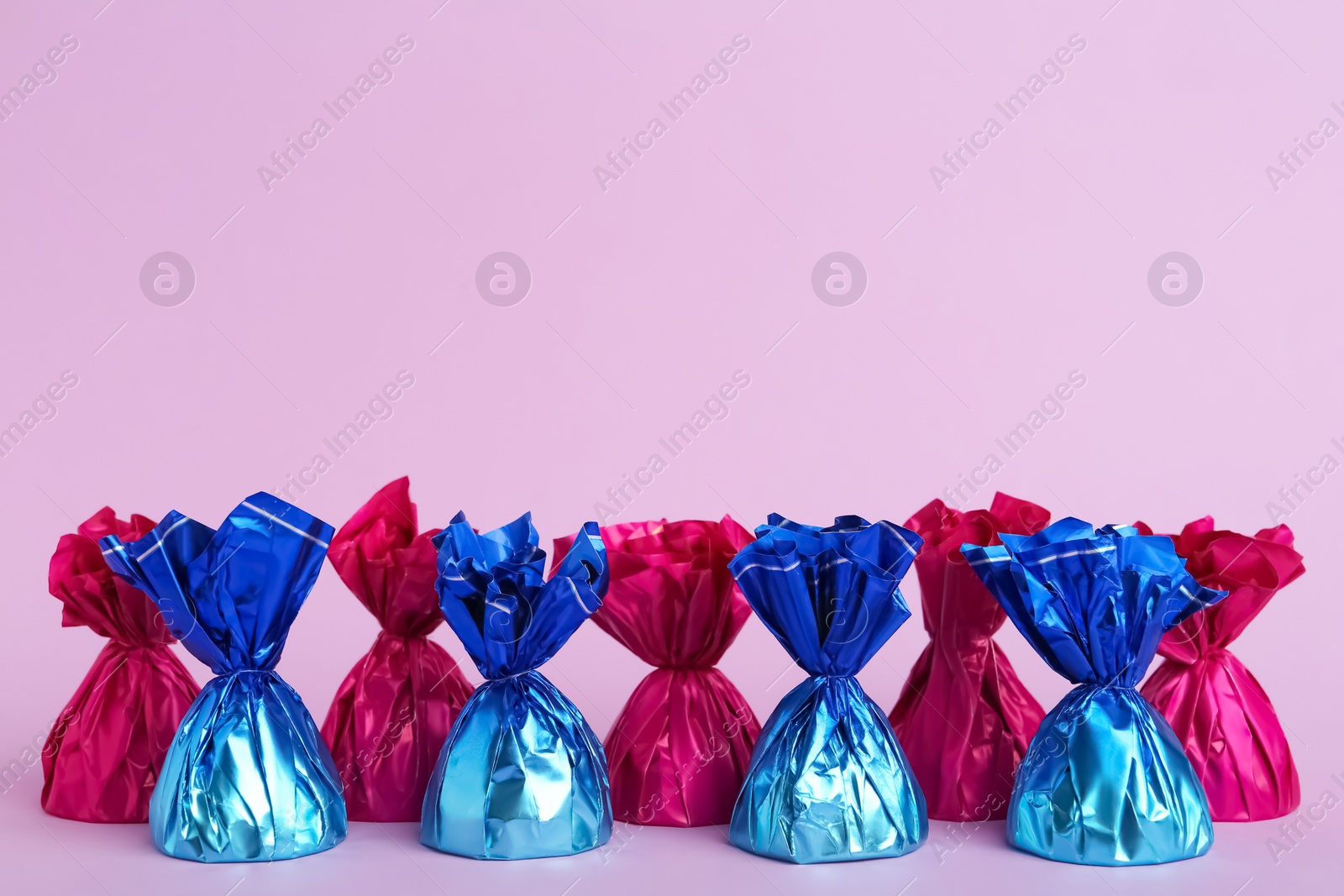 Photo of Candies in colorful wrappers on pink background. Space for text