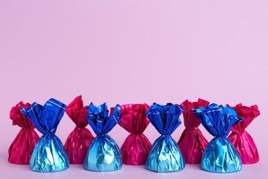 Photo of Candies in colorful wrappers on pink background. Space for text